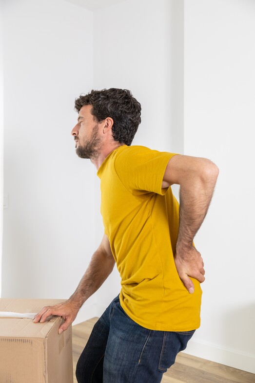 Person standing and holding their lower back in pain while lifting a box, illustrating a common lumbar disc injury scenario.