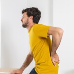Person standing and holding their lower back in pain while lifting a box, illustrating a common lumbar disc injury scenario.